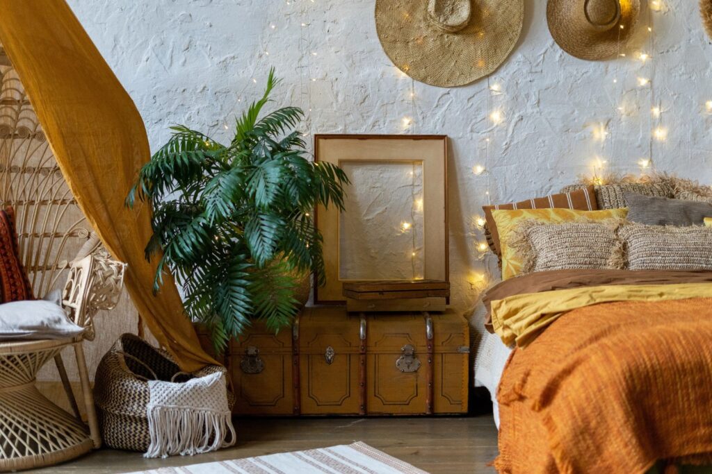 ultra cozy bedroom with warm colored bedcovers, string lights, a plant, rug, and basket with a blanket